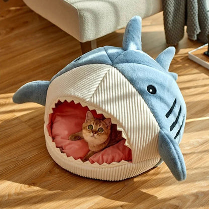 Cat lying inside a shark-shaped pet bed on a wooden floor.