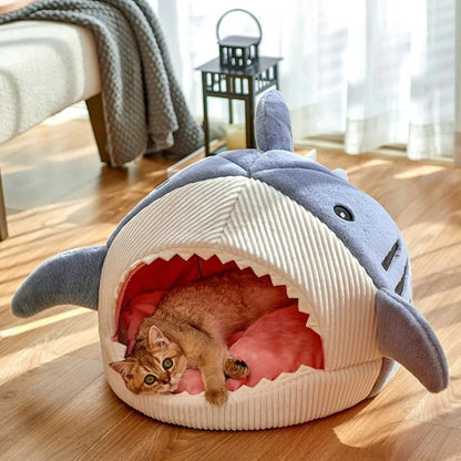 Cat lying in a shark-shaped pet bed on a wooden floor.