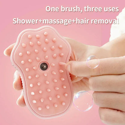 Pink silicone brush held by a hand with bubbles on a pink background, labeled 'One brush, three uses: Shower + massage + hair removal'.